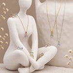 November blue topaz initial necklaces in silver, gold and rose gold on white ceramic displays, taupe background