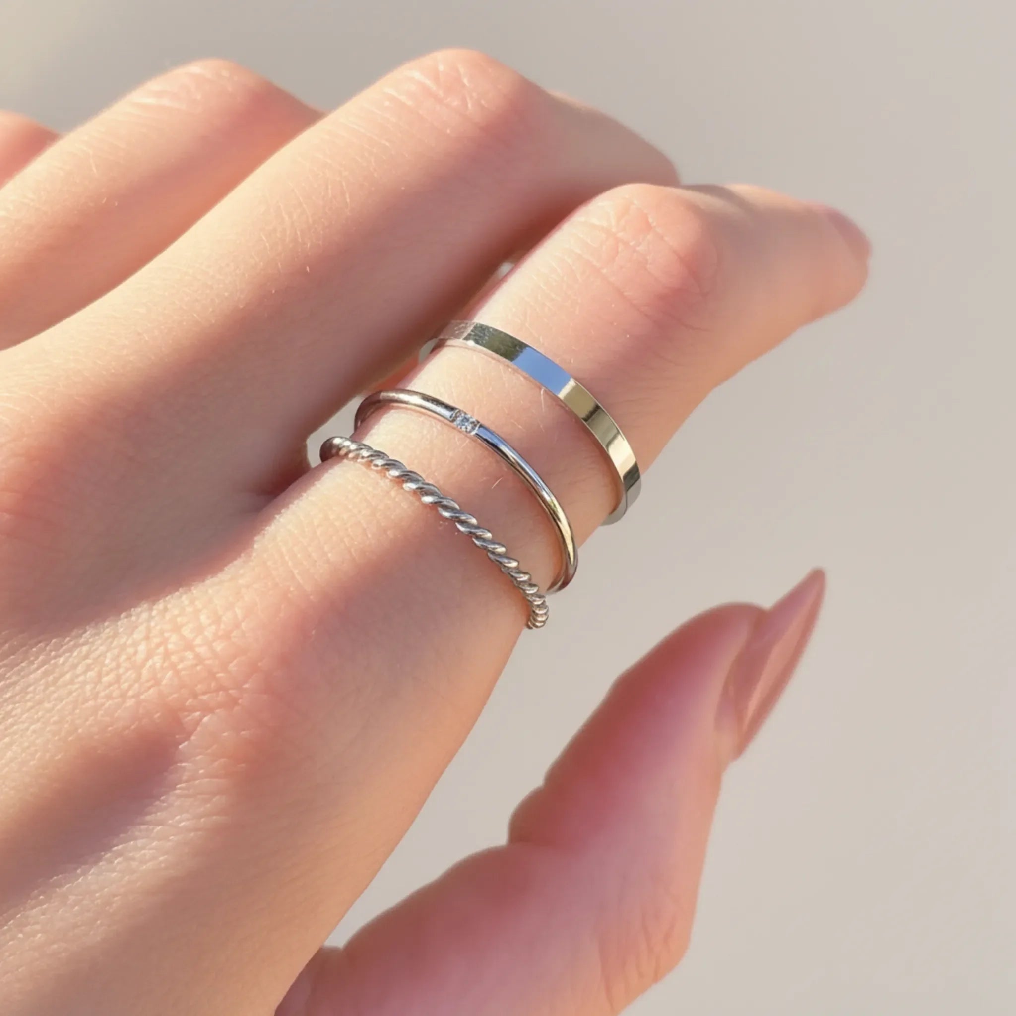 Hand wearing three silver stacker rings with a light background