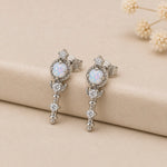 Pair of silver stud earrings with white opal stones and CZs on a beige surface