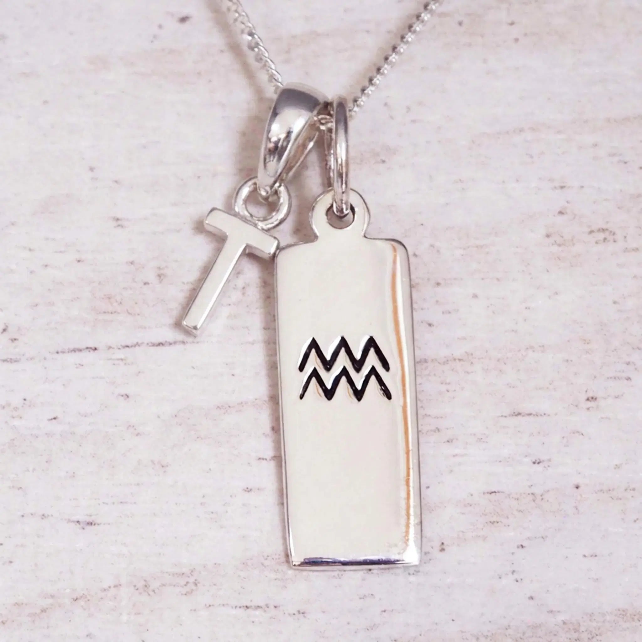 Sterling Silver T Initial and Aquarius Necklace on a fine silver chain against a light wooden background