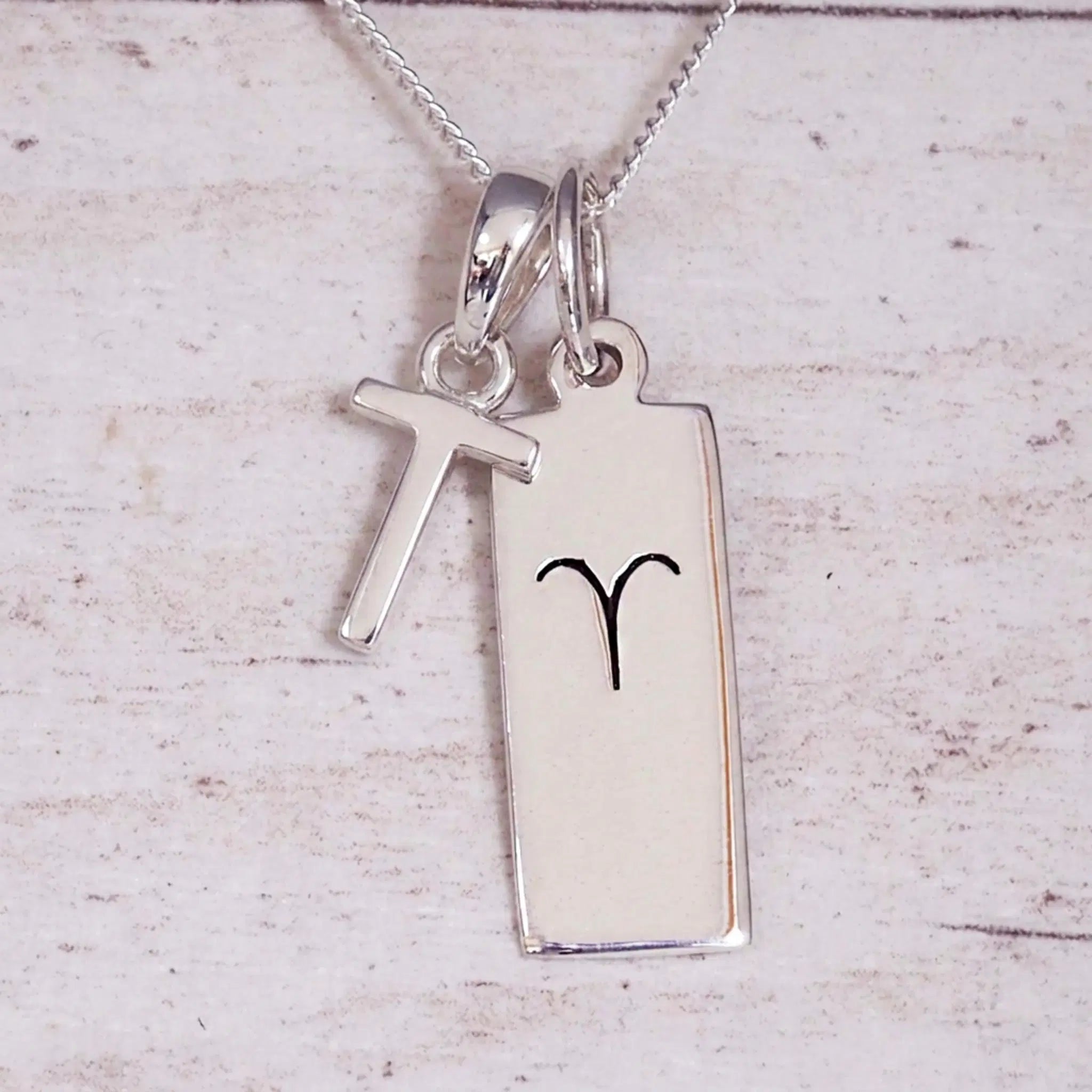 Sterling Silver T Initial pendant and Aries necklace on a fine silver chain on a light wooden background