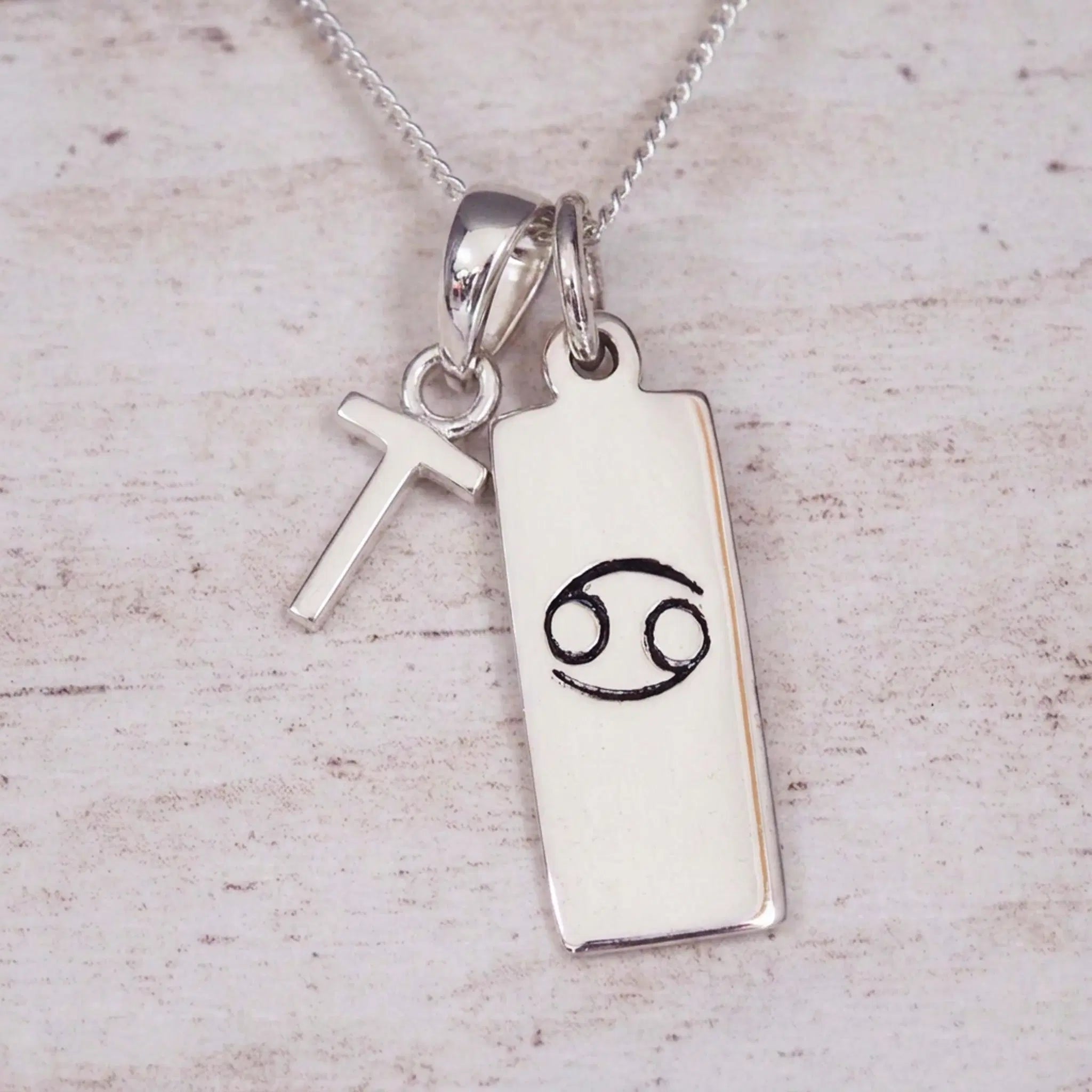 Sterling Silver T Initial Cancer Zodiac Star Sign Necklace on a fine silver chain against a light wooden background