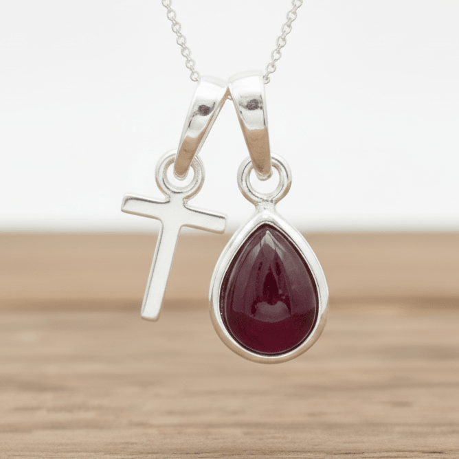 Silver t initial necklace with a teardrop-shaped red ruby gemstone pendant on a wooden surface.