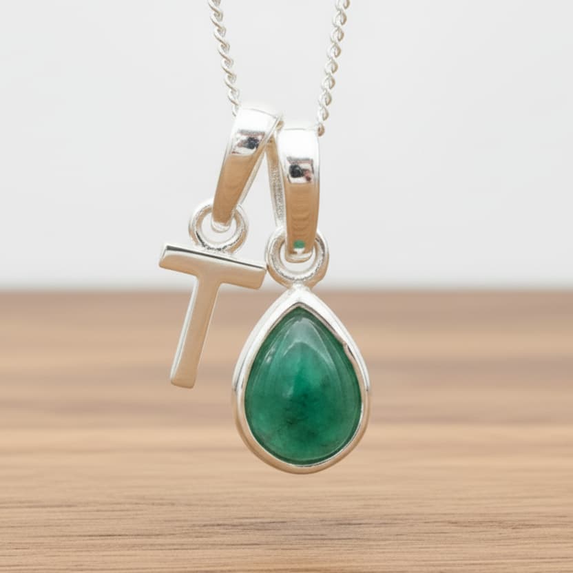 Silver Initial T necklace with a teardrop-shaped Emerald gemstone pendant hanging above a rustic wooden surface
