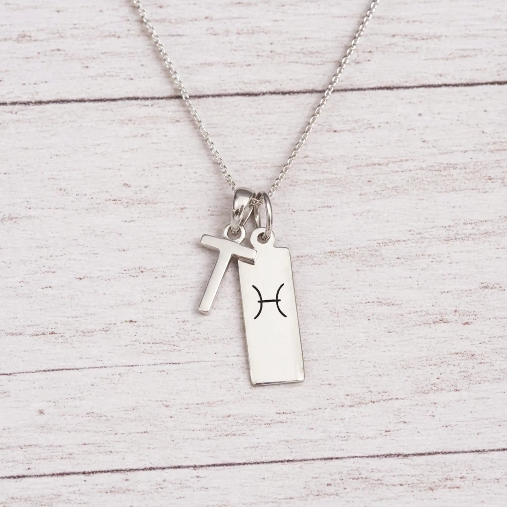sterling silver T initial Pisces Necklace on a fine silver chain against a light wooden background