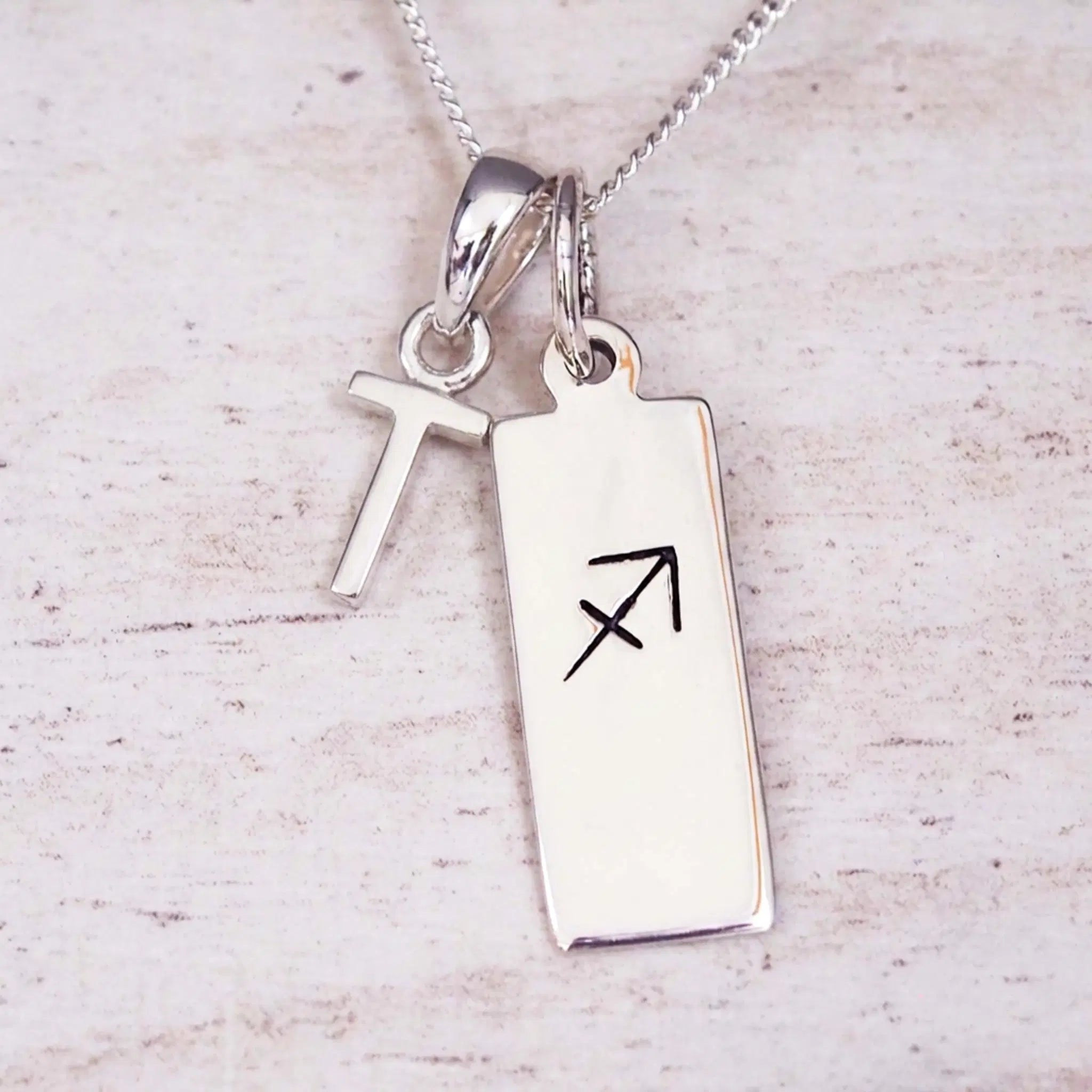 sterling silver initial t sagittarius zodiac star sign pendant necklace against a light wooden background