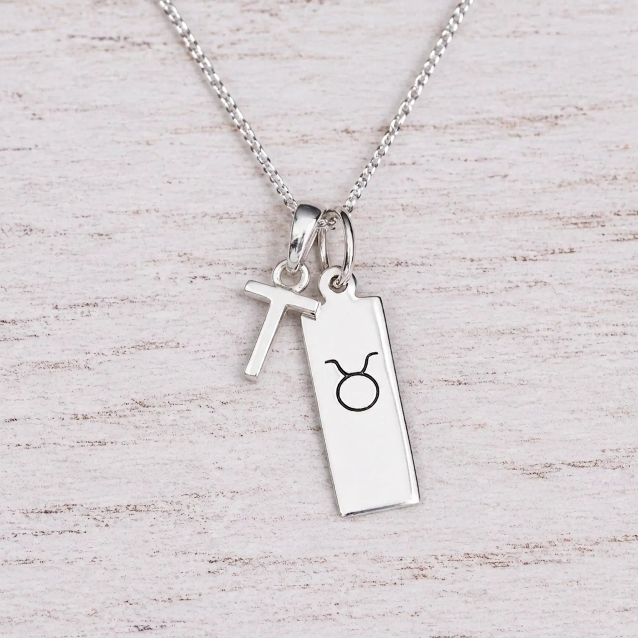 Sterling silver T initial Pendant and Taurus Necklace on a fine silver chain on a light wooden background
