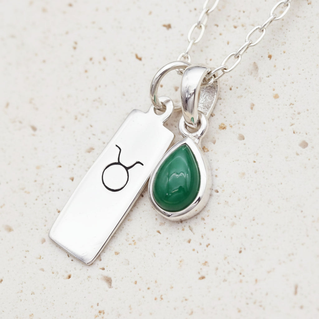 Silver necklace with Taurus zodiac symbol and green natural emerald gemstone teardrop pendant on a textured surface