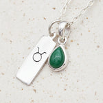 sterling silver Necklace with Taurus zodiac pendant and a teardrop May birthstone emerald pendant on a textured background