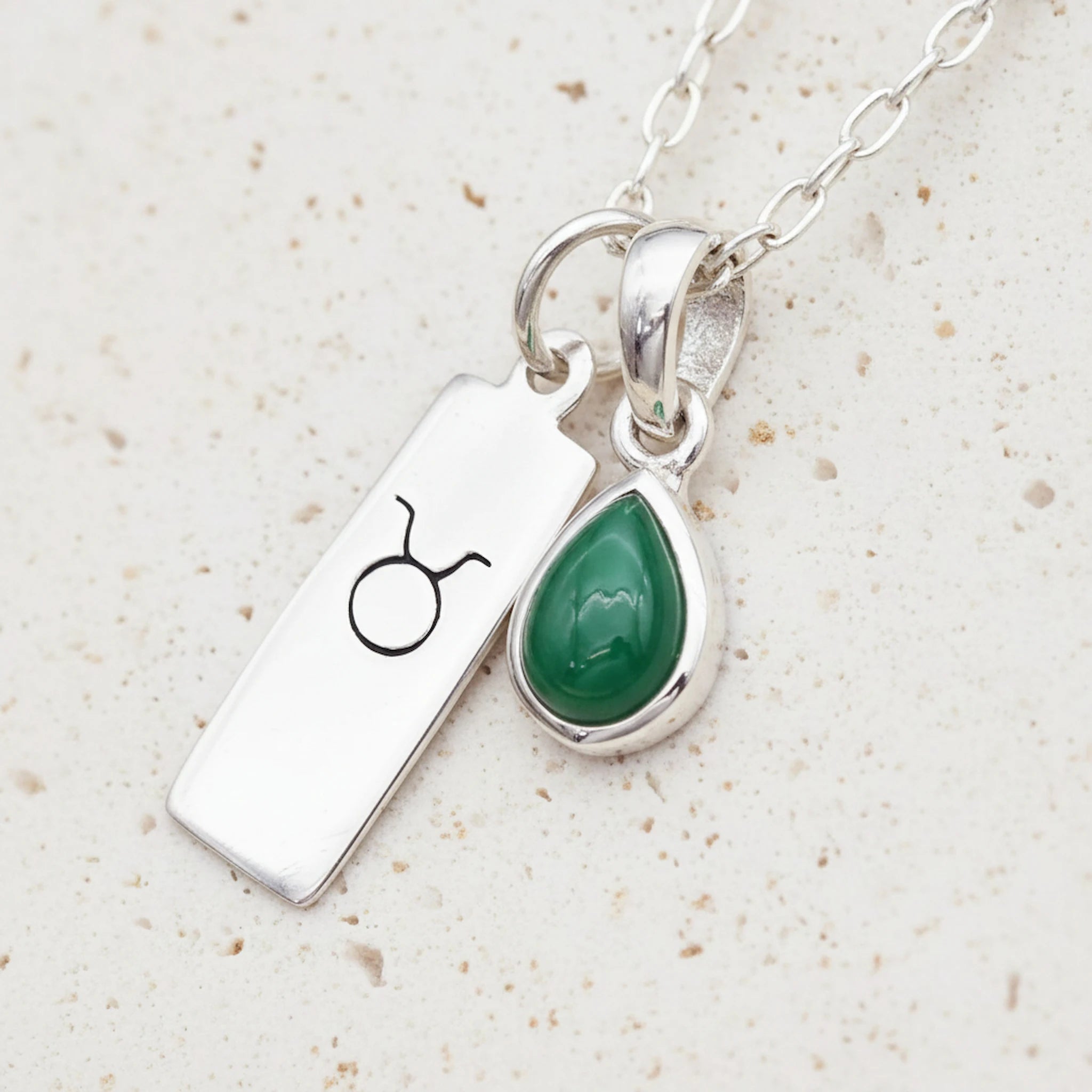 sterling silver Necklace with Taurus zodiac pendant and a teardrop May birthstone emerald pendant on a textured background