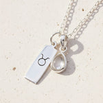 Sterling Silver necklace with april birthstone herkimer quartz pendant and a Taurus zodiac pendant on a beige surface