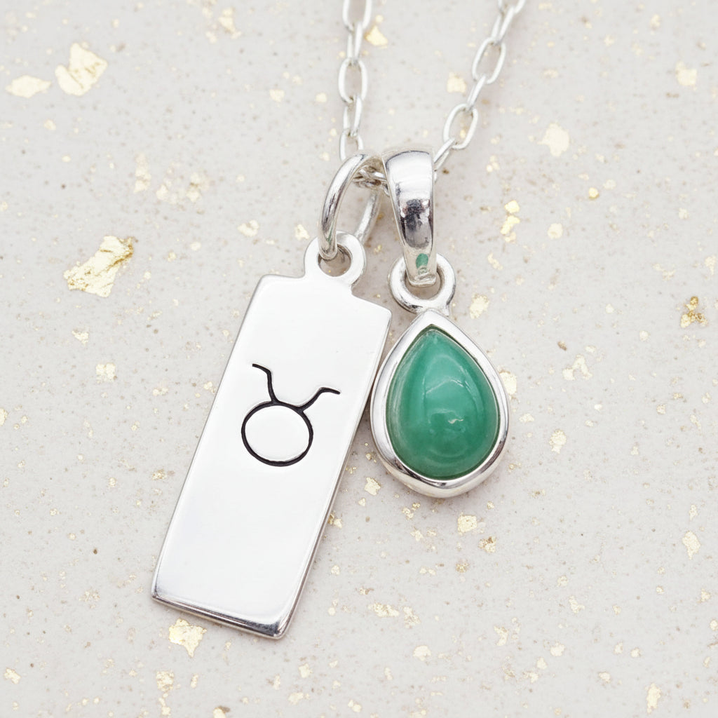 Sterling Silver Zodiac Taurus pendant and May Birthstone Emerald pendant on a textured surface