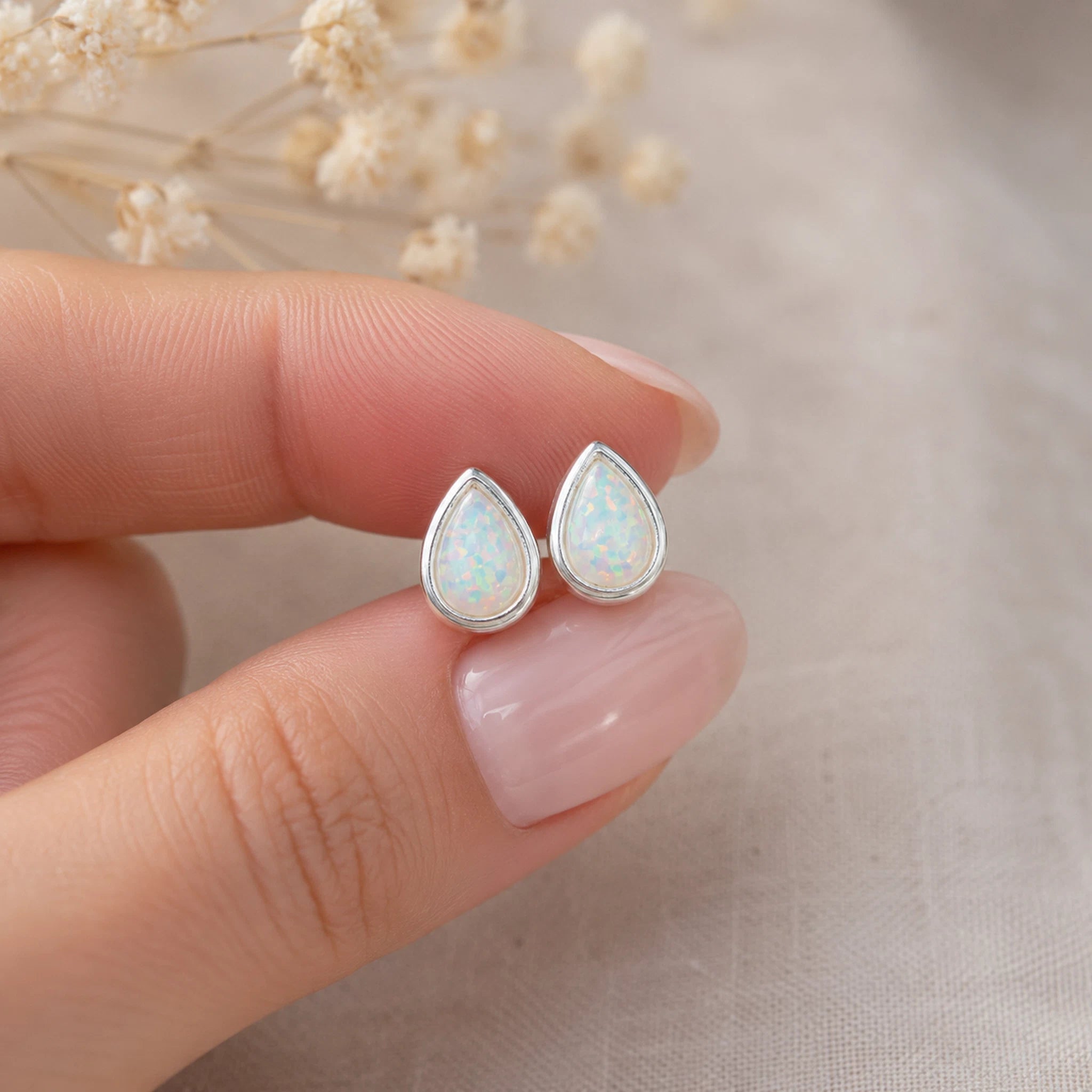 sterling silver stud earrings with teardrop bezel set white opals being held