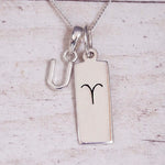 Sterling Silver U Initial pendant and Aries necklace on a fine silver chain on a light wooden background