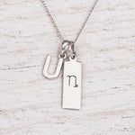 sterling silver initial U pendant and capricorn necklace on a fine silver chain against a light wooden background