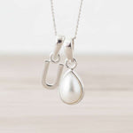 Silver necklace with a u initial pendant and a teardrop-shaped pearl pendant on a light background