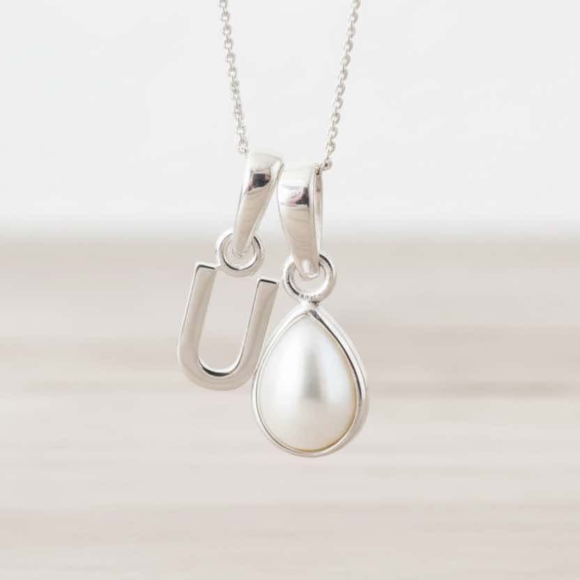 Silver necklace with a u initial pendant and a teardrop-shaped pearl pendant on a light background
