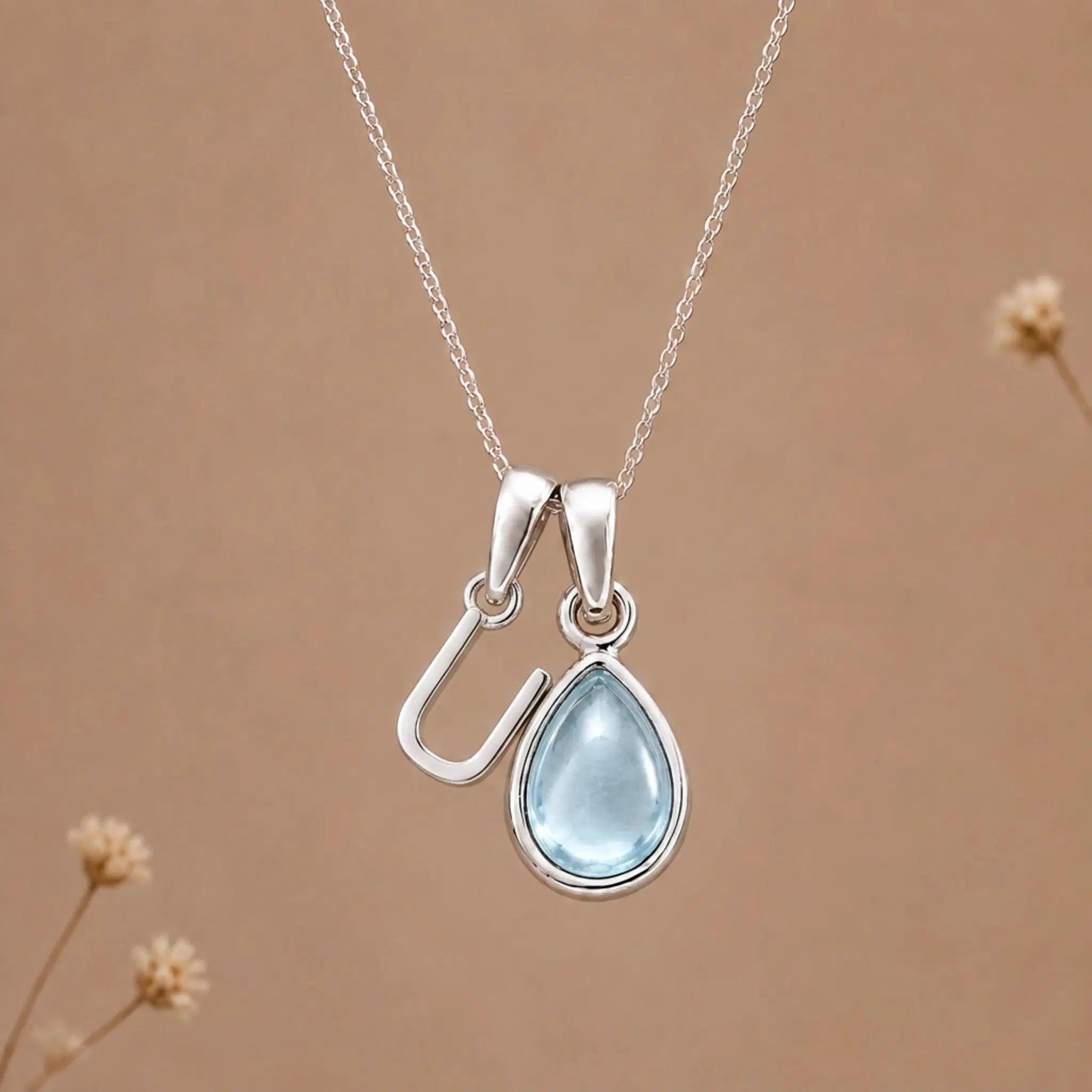 sterling silver initial u march birthstone natural aquamarine pendant necklace against a dark warm beige background