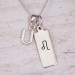 sterling silver initial u leo zodiac star sign pendant necklace against a light wooden background