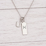 sterling silver U initial Pisces Necklace on a fine silver chain against a light wooden background