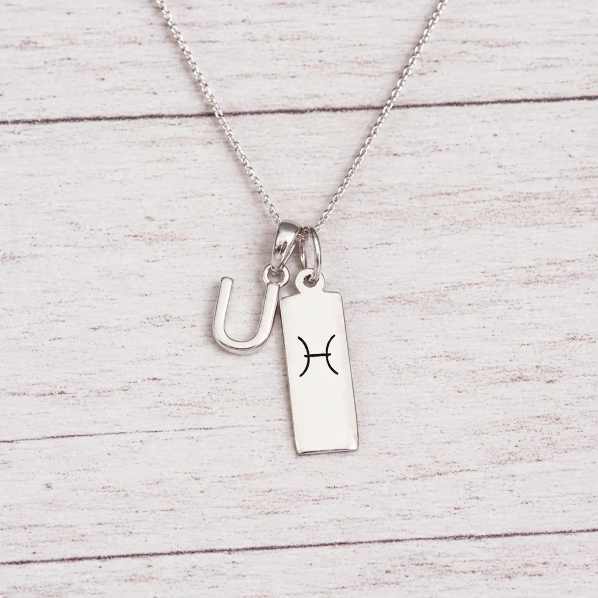 sterling silver U initial Pisces Necklace on a fine silver chain against a light wooden background