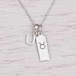 Sterling silver U initial Pendant and Taurus Necklace on a fine silver chain on a light wooden background