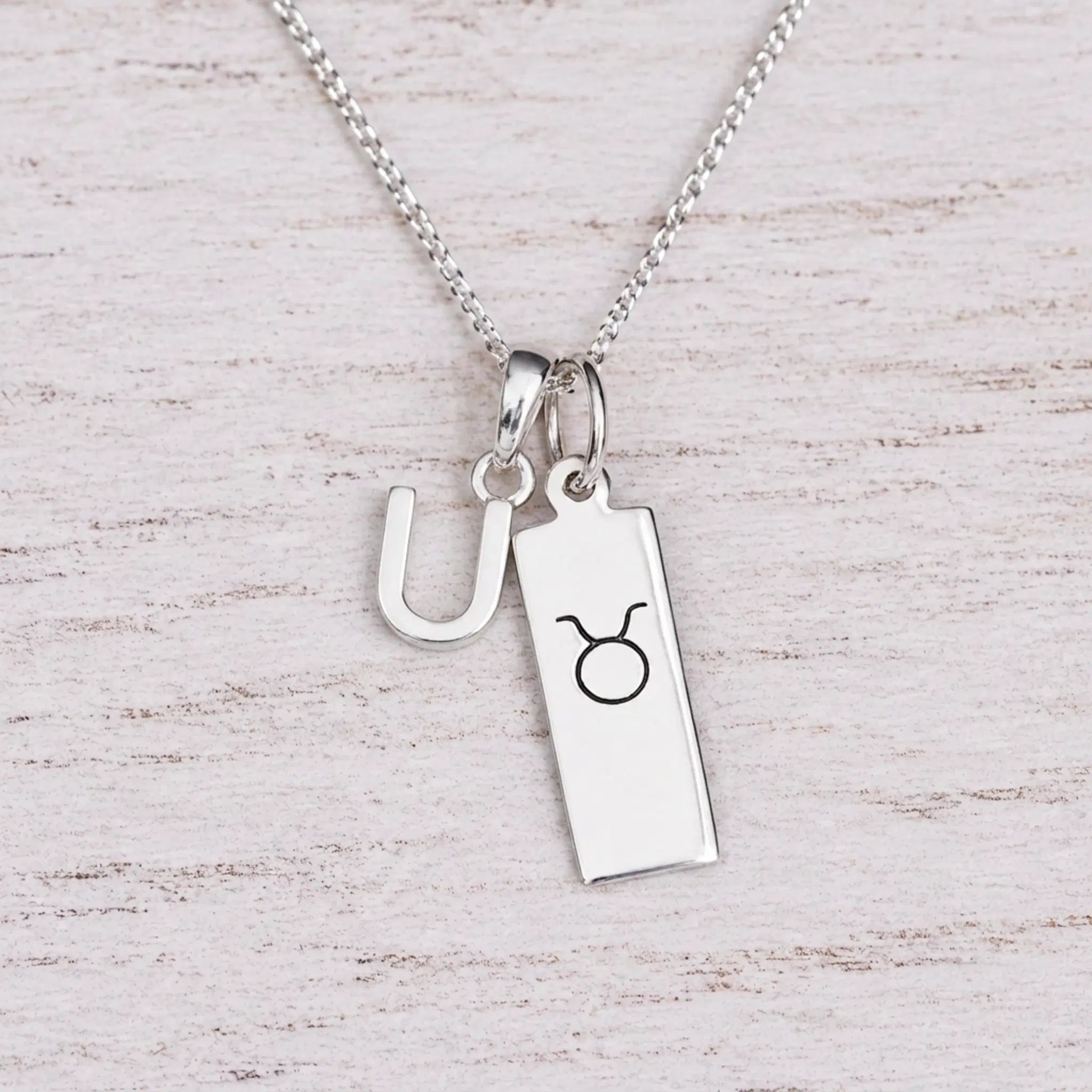 Sterling silver U initial Pendant and Taurus Necklace on a fine silver chain on a light wooden background