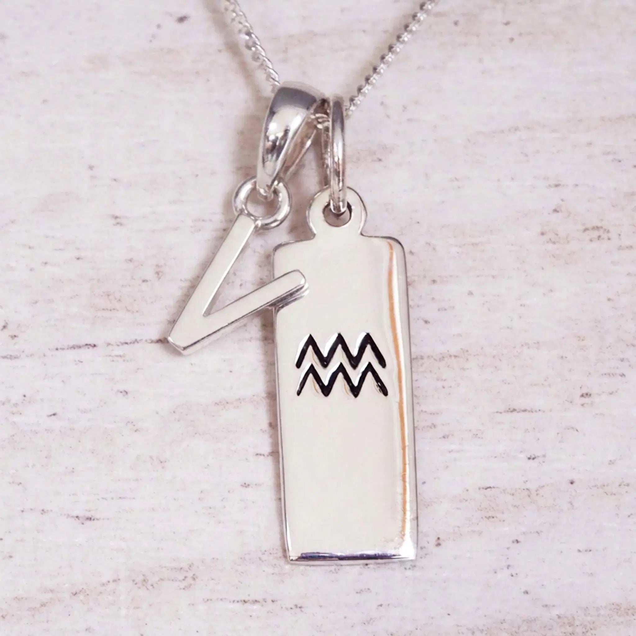 Sterling Silver V Initial and Aquarius Necklace on a fine silver chain against a light wooden background