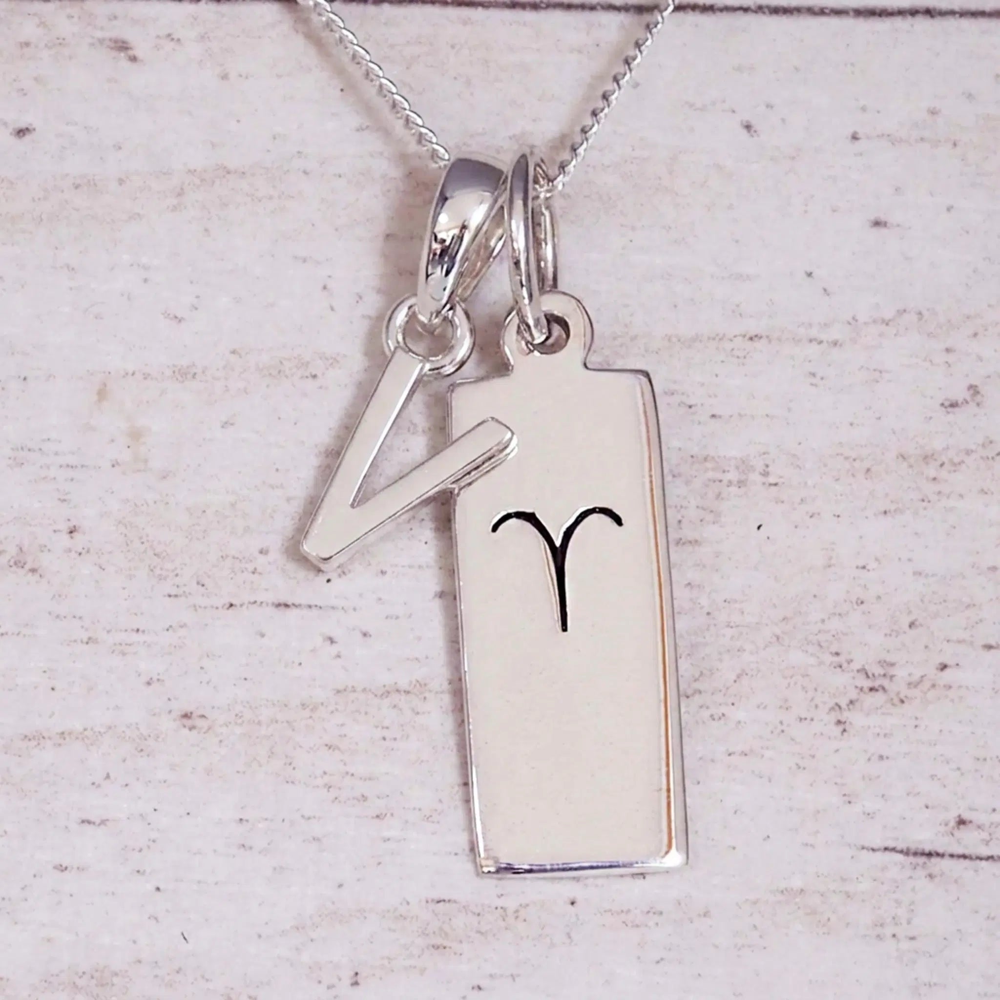 Sterling Silver V Initial pendant and Aries necklace on a fine silver chain on a light wooden background