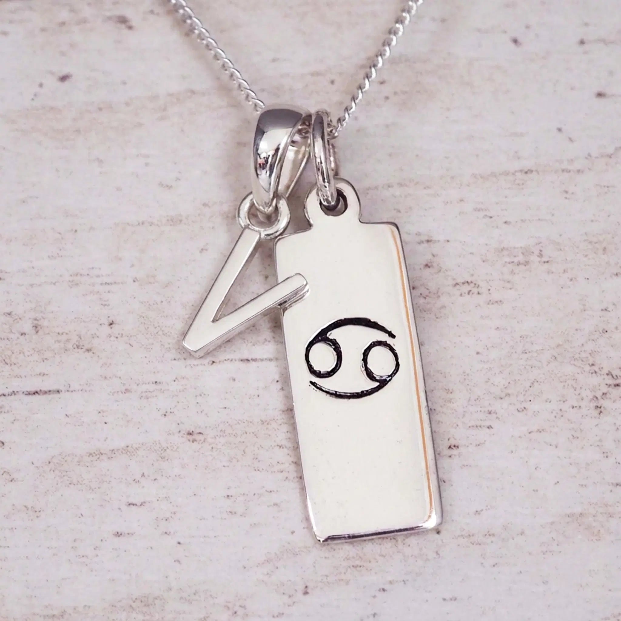 Sterling Silver V Initial Cancer Zodiac Star Sign Necklace on a fine silver chain against a light wooden background