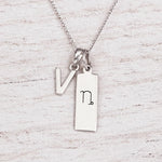 sterling silver initial V pendant and capricorn necklace on a fine silver chain against a light wooden background