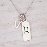 Sterling silver V initial and GeminI Necklace on a fine silver chain on a light wooden background