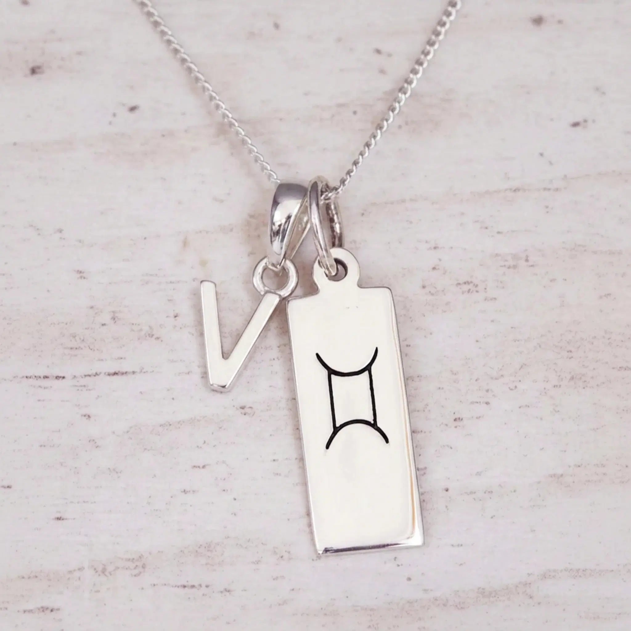 Sterling silver V initial and GeminI Necklace on a fine silver chain on a light wooden background