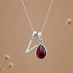 sterling silver initial v january birthstone natural garnet pendant necklace against a dark warm beige background