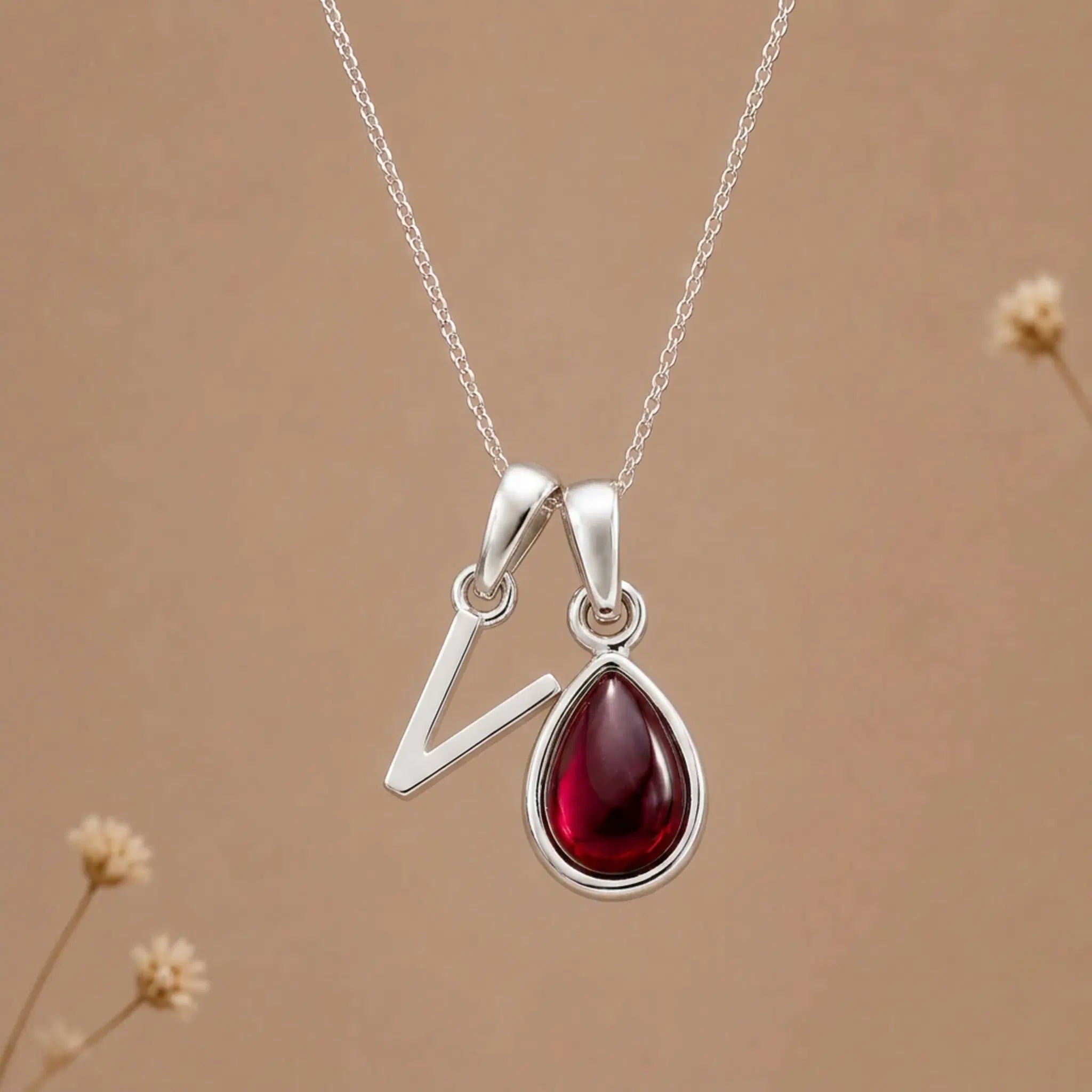 sterling silver initial v january birthstone natural garnet pendant necklace against a dark warm beige background