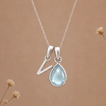 sterling silver initial v march birthstone natural aquamarine pendant necklace against a dark warm beige background