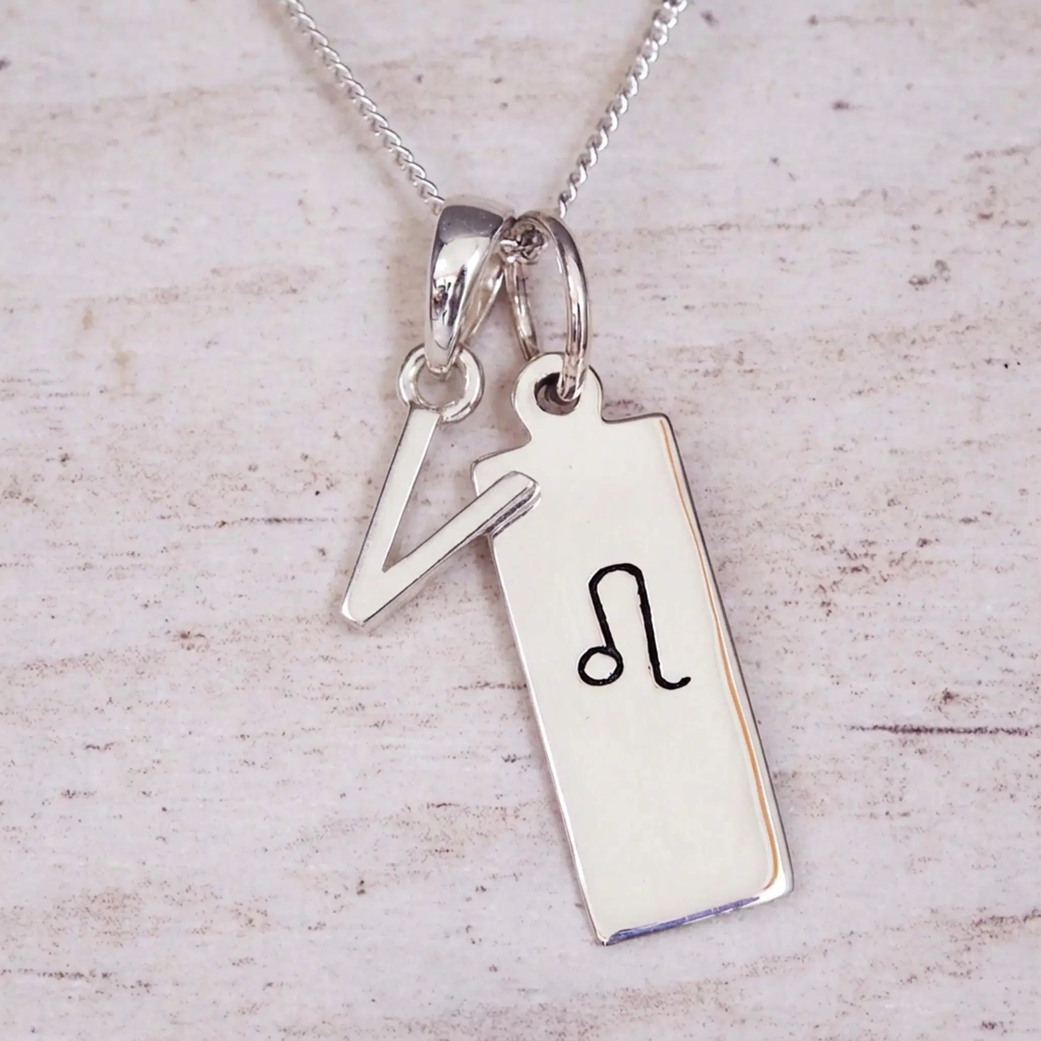 sterling silver initial v leo zodiac star sign pendant necklace against a light wooden background