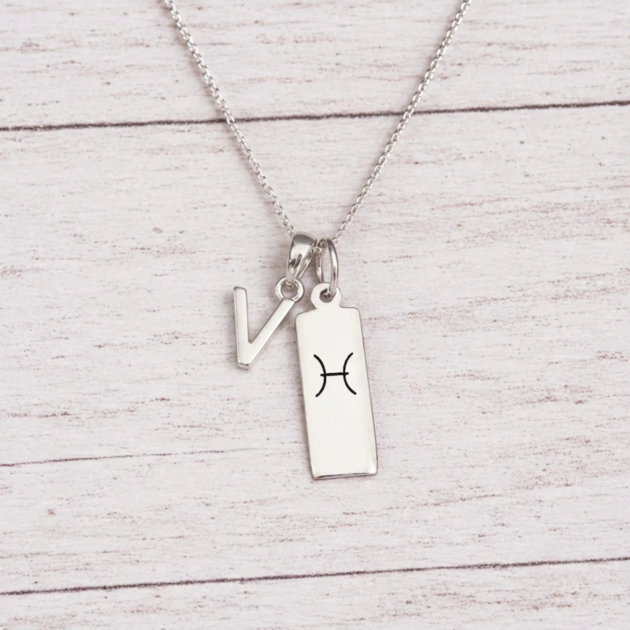 sterling silver V initial Pisces Necklace on a fine silver chain against a light wooden background