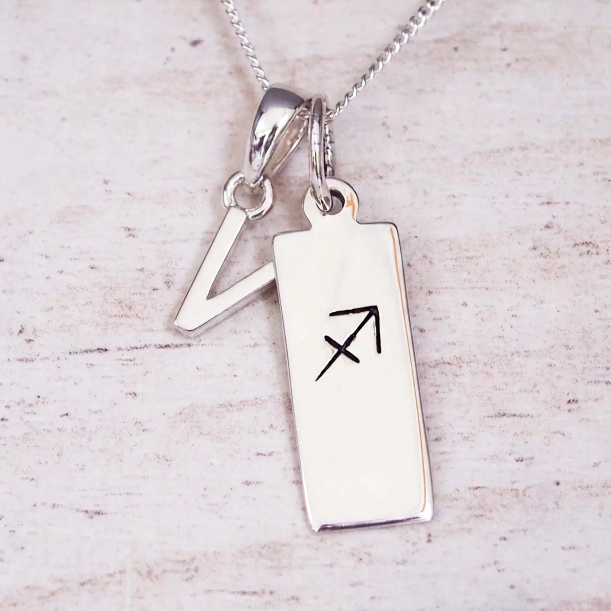 sterling silver initial v sagittarius zodiac star sign pendant necklace against a light wooden background