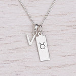 Sterling silver V initial Pendant and Taurus Necklace on a fine silver chain on a light wooden background