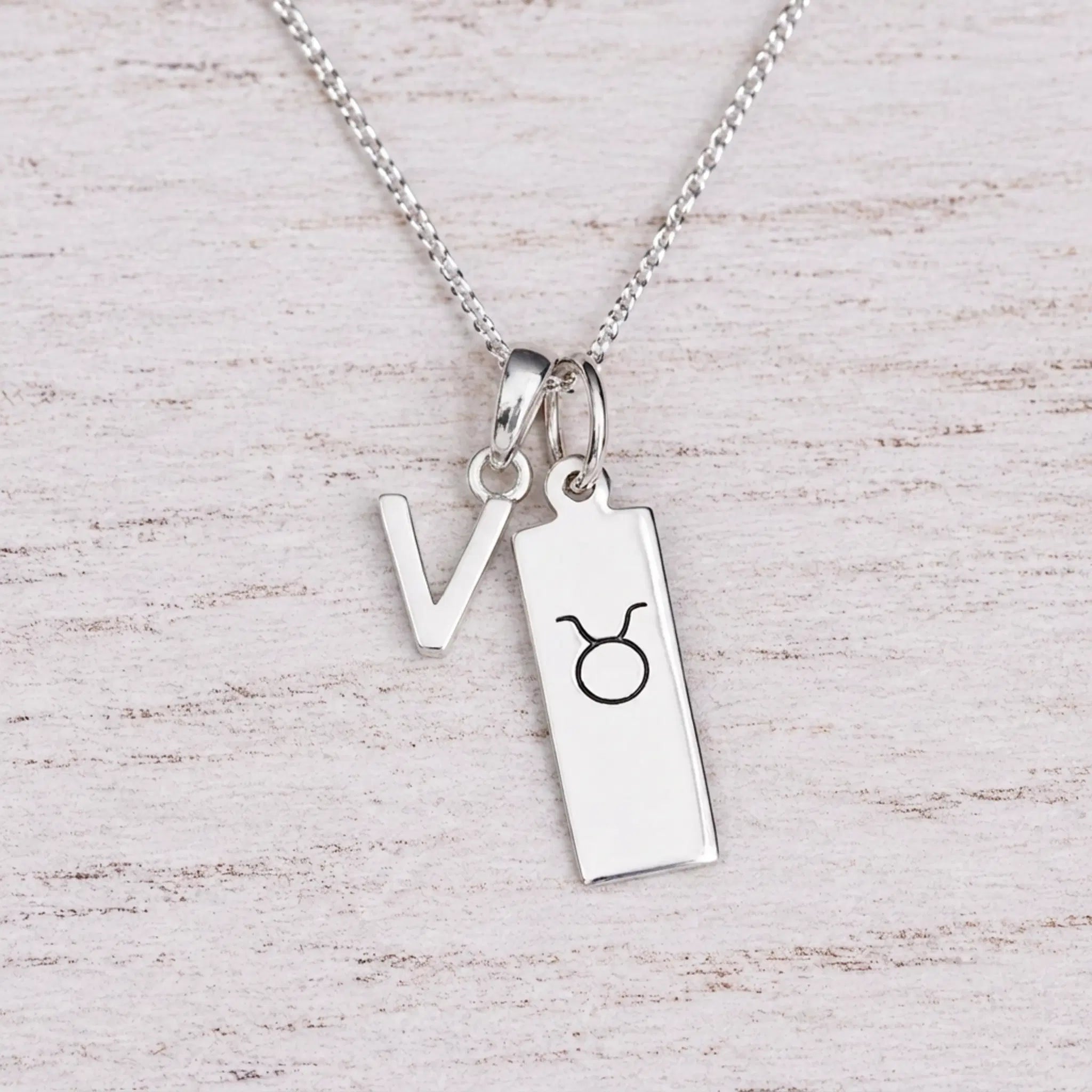 Sterling silver V initial Pendant and Taurus Necklace on a fine silver chain on a light wooden background
