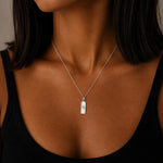 virgo zodiac necklace - A close-up of a woman wearing a delicate silver chain necklace with a small rectangular pendant engraved with the virgo star sign line glyph.