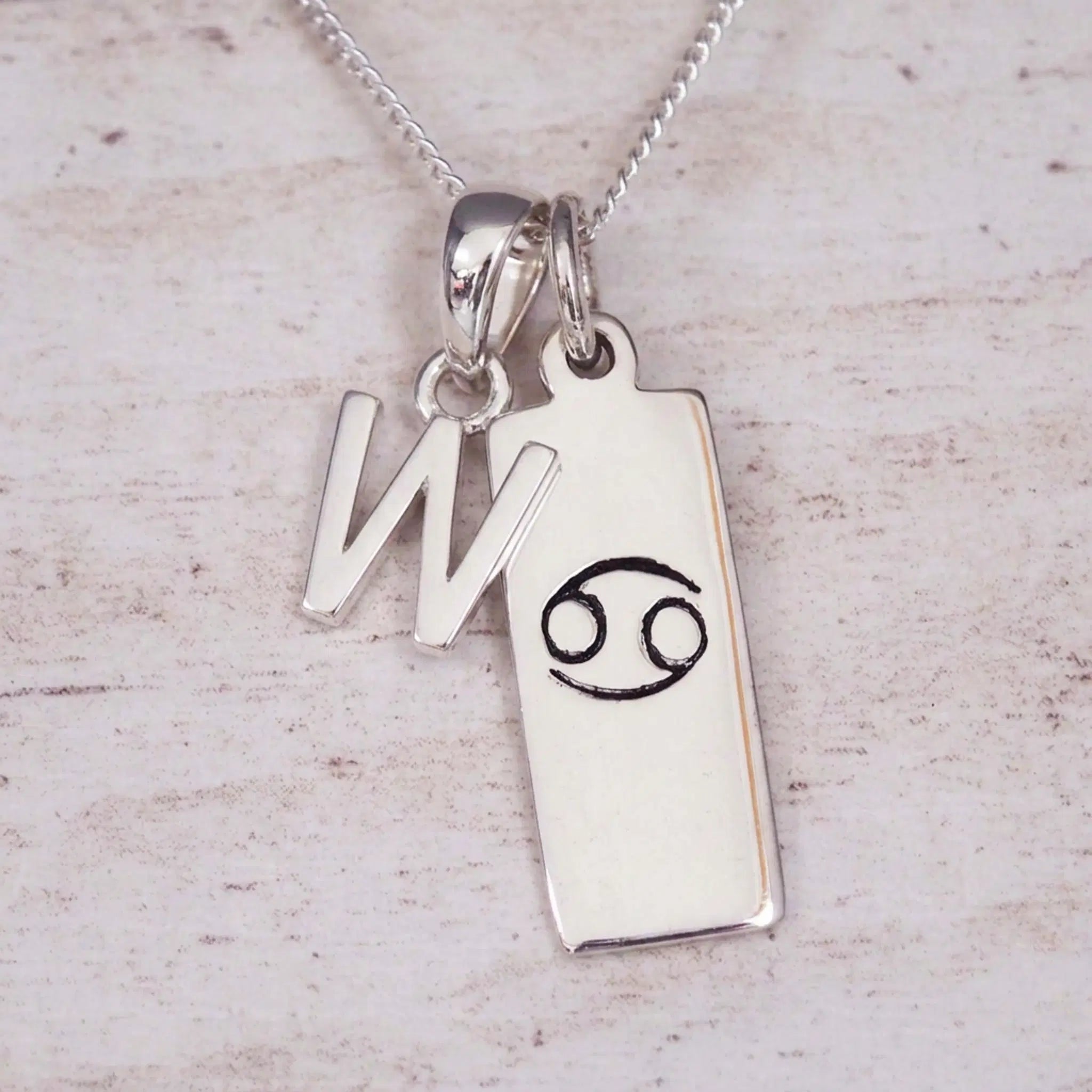 Sterling Silver W Initial Cancer Zodiac Star Sign Necklace on a fine silver chain against a light wooden background