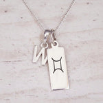 Sterling silver W initial and GeminI Necklace on a fine silver chain on a light wooden background