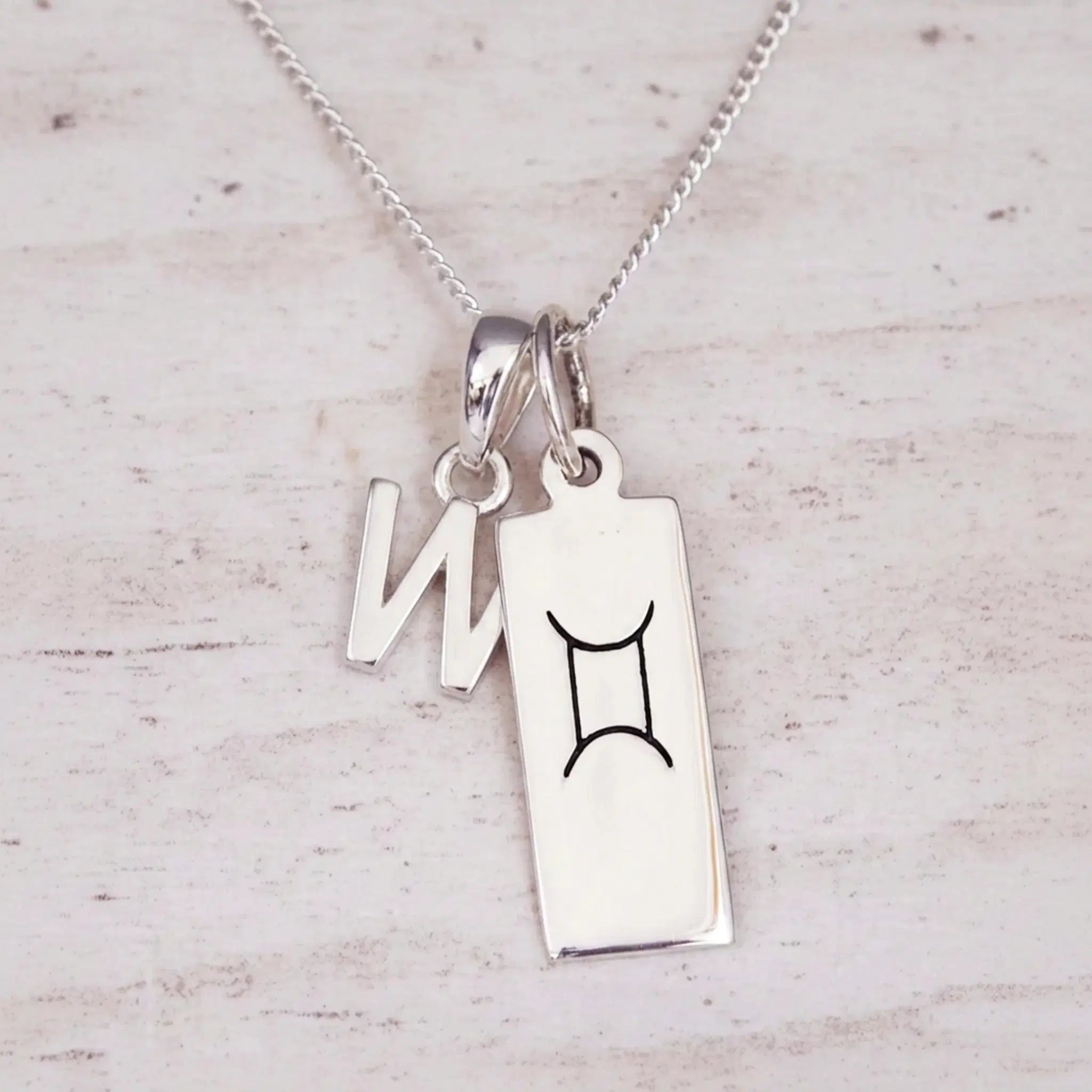 Sterling silver W initial and GeminI Necklace on a fine silver chain on a light wooden background
