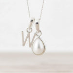 Silver necklace with a 'W' pendant and a teardrop-shaped pearl on a light background