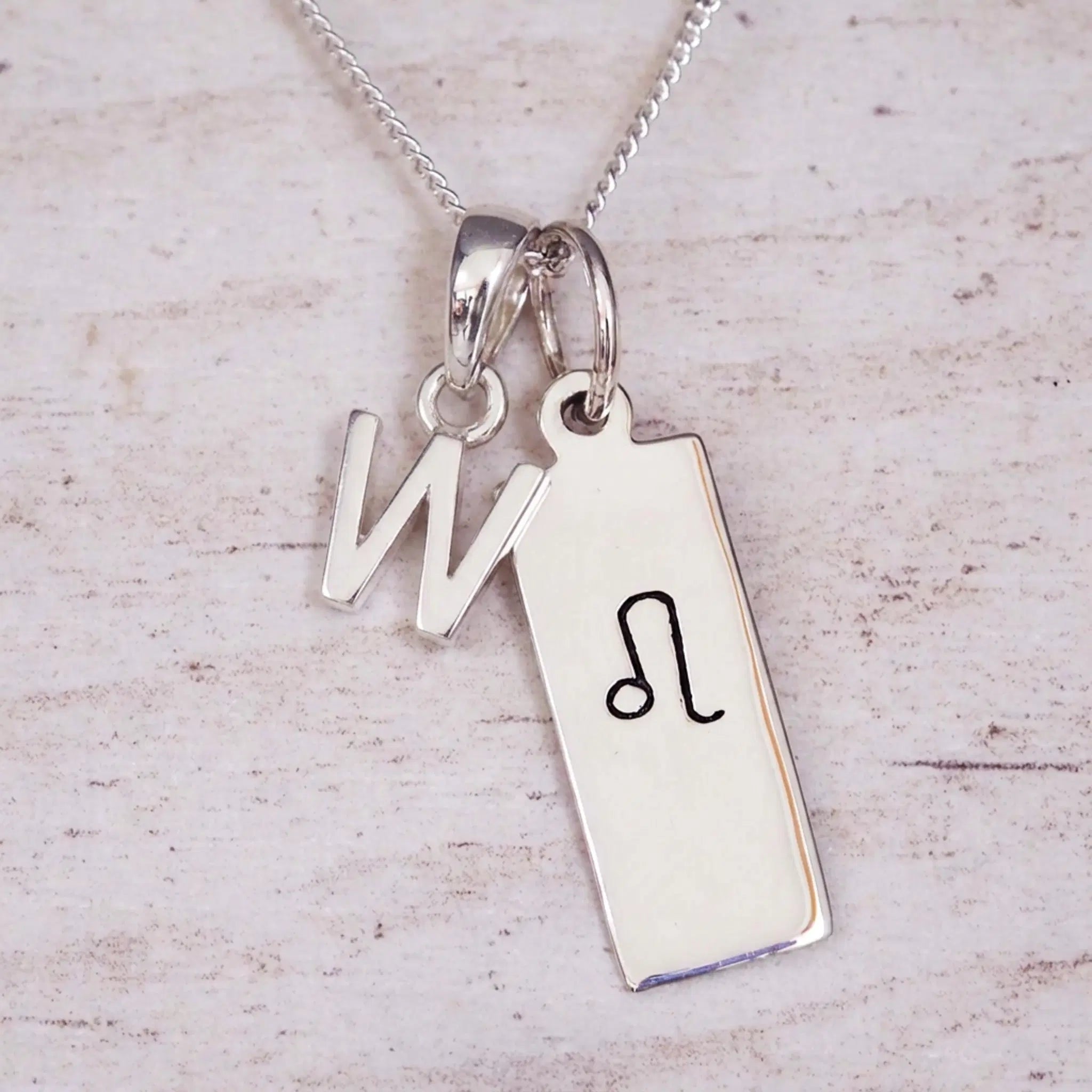 sterling silver initial w leo zodiac star sign pendant necklace against a light wooden background