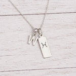 sterling silver W initial Pisces Necklace on a fine silver chain against a light wooden background