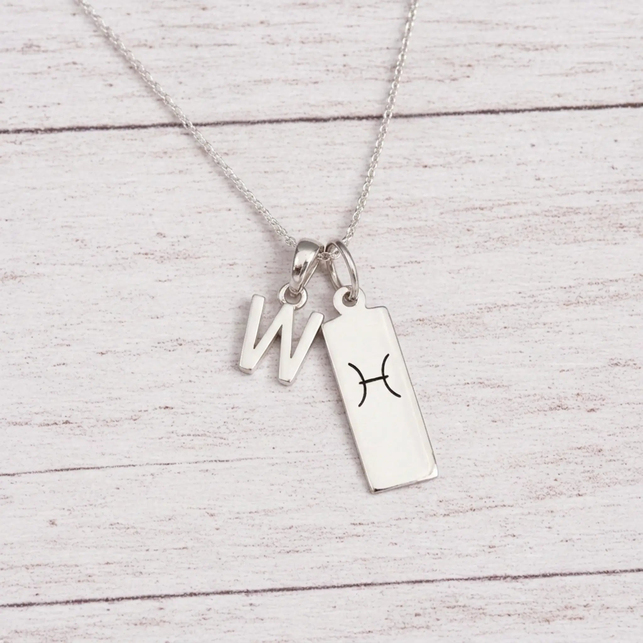 sterling silver W initial Pisces Necklace on a fine silver chain against a light wooden background