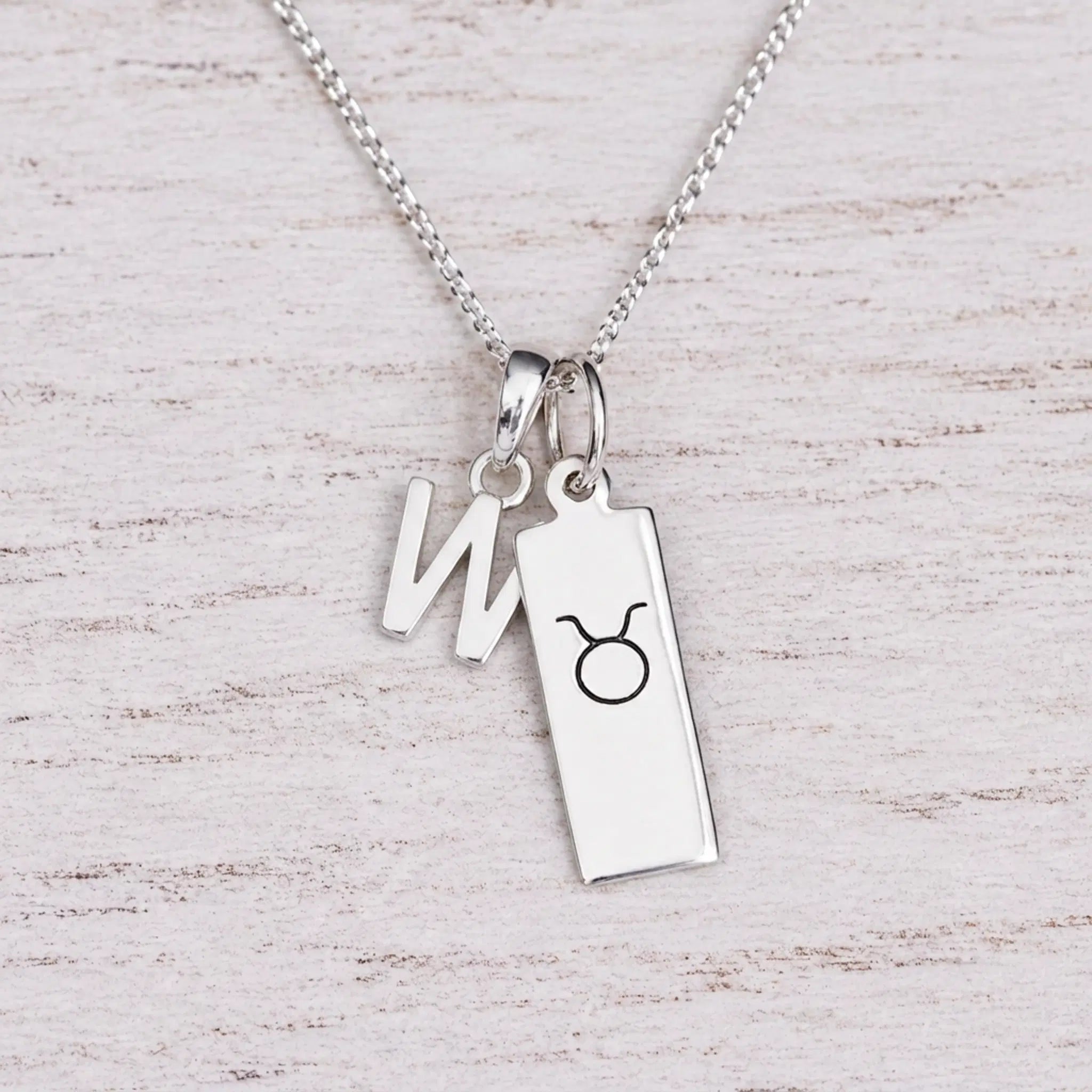 Sterling silver W initial Pendant and Taurus Necklace on a fine silver chain on a light wooden background